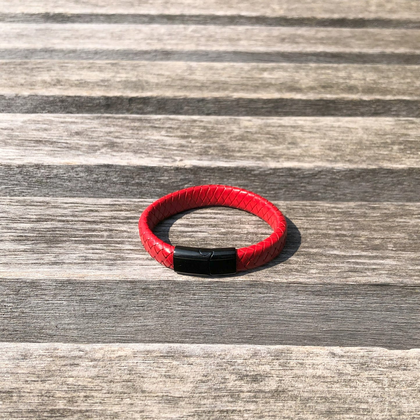 Red bracelet with a black clasp on a wooden surface