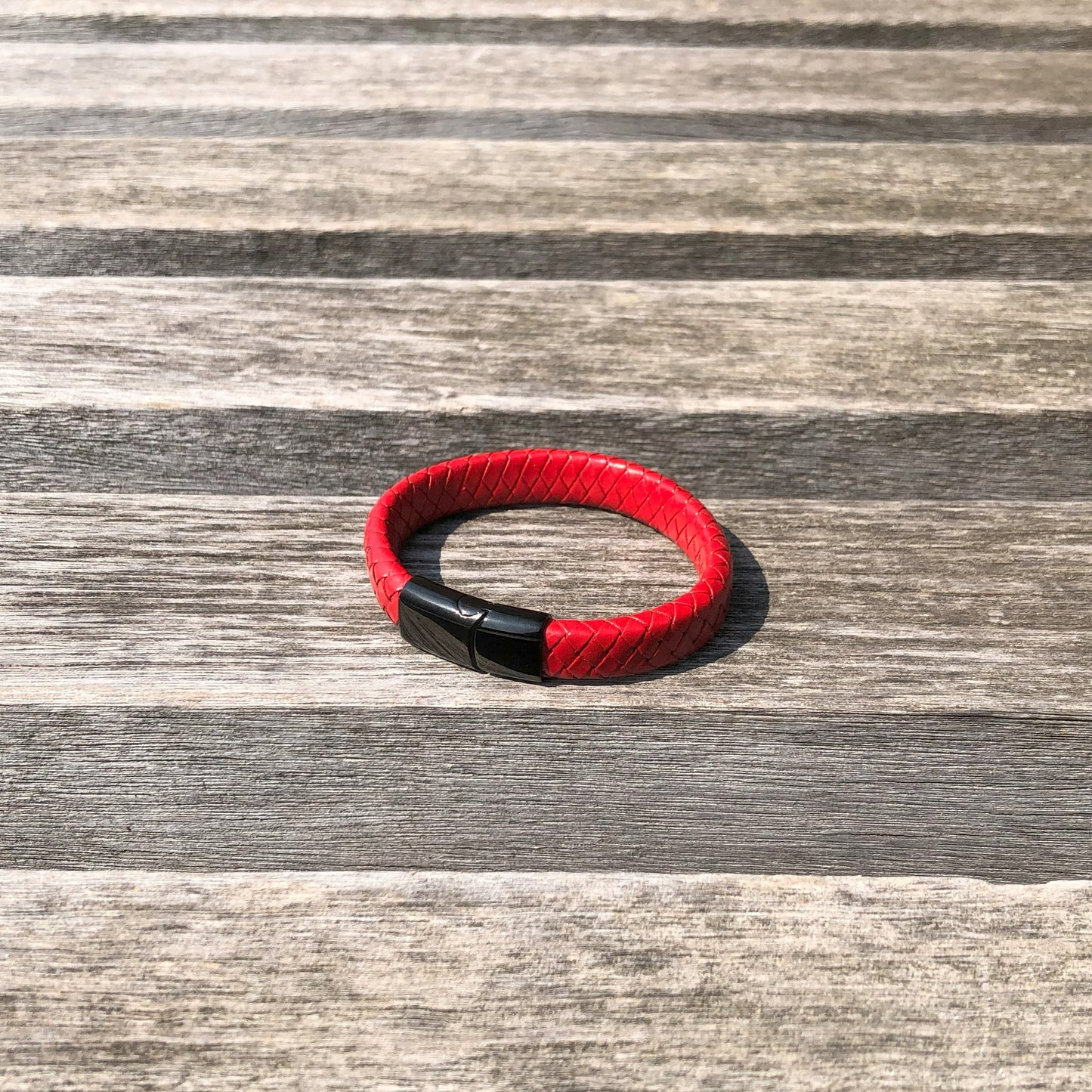 Red braided bracelet with a black clasp on a wooden surface