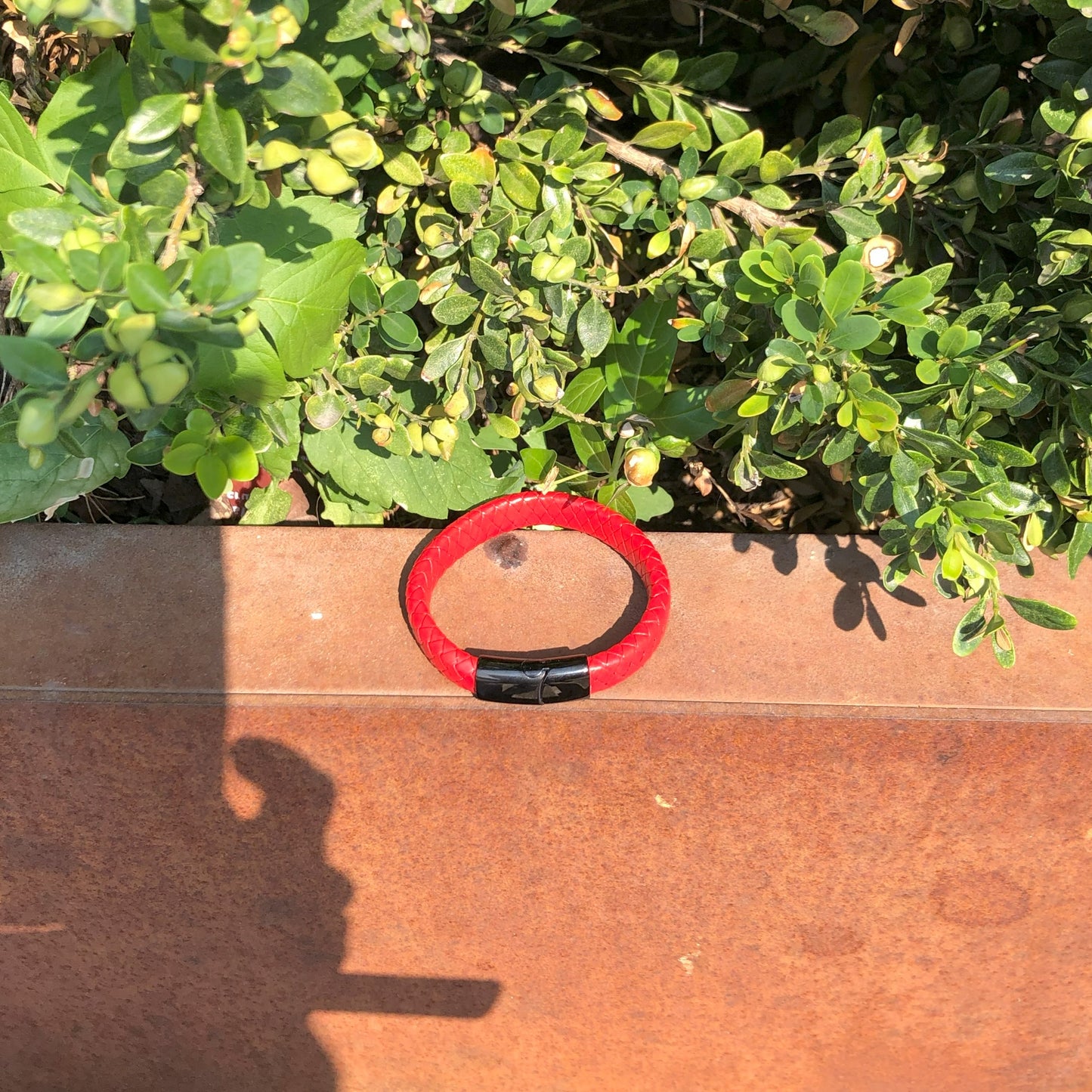 Red and black bracelet on a wooden surface with green foliage in the background